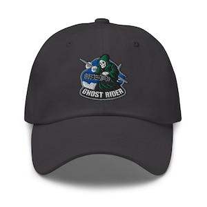Puede incluir: Gorra de béisbol gris oscuro con un parche bordado. El parche representa una figura de la Parca verde y el texto "GHOST RIDER" en blanco. El diseño incluye detalles en azul y blanco.