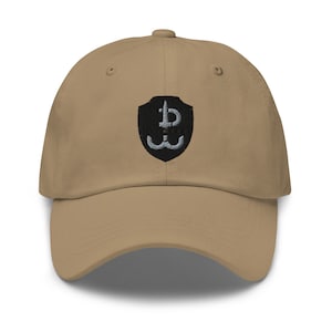 Puede incluir: Una gorra de béisbol de color beige con un parche bordado en negro que presenta una espada y las letras "P" y "W" dentro de un escudo.