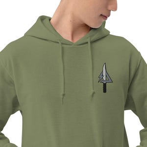 May include: Olive green hooded sweatshirt with a small embroidered design of a knife and lightning bolt. The design is in shades of gray and black. The sweatshirt has a drawstring hood and a kangaroo pocket.