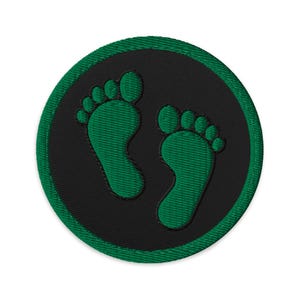 Può includere: Toppa ricamata con due impronte di piedi verdi su sfondo circolare nero, incorniciata da un bordo verde. Il design è semplice e pulito, adatto a varie applicazioni.
