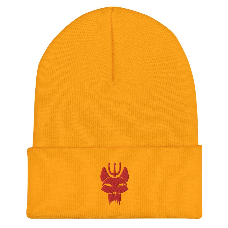 Puede incluir: Un gorro de punto amarillo con un logotipo rojo bordado de una cabeza de animal estilizada con un tridente en la parte superior.