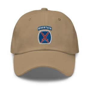May include: A tan baseball cap with an embroidered patch featuring a blue shield with crossed swords and the text "MOUNTAIN".