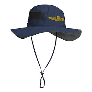 May include: Navy blue sun hat with a wide brim and a black mesh panel. The hat features a gold-colored parachute and wing emblem on the side and an adjustable chin strap. The brim is approximately 3 inches wide.