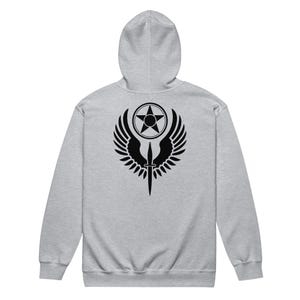 Könnte beinhalten: Ein hellgrauer Kapuzenpullover mit einem schwarzen Aufdruck auf dem Rücken. Der Aufdruck zeigt einen Stern in einem Kreis, flankiert von Flügeln und einem nach unten zeigenden Dolch. Der Hoodie hat eine Kapuze und eine Kängurutasche.