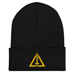 Peut inclure: Bonnet noir avec un motif brodé jaune représentant un triangle et une croix. Le bonnet est fait d'une matière tricotée douce et possède un bord replié. Le motif est centré sur le devant du bonnet.