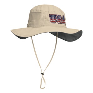 May include: A beige sun hat with a wide brim and a black chin strap. The hat has a mesh panel on the top and the word "USA" embroidered on the front in red, white, and blue.