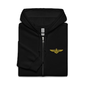 May include: Black zip-up hooded sweatshirt with a gold embroidered emblem on the chest. The emblem features a shield, wings, and other details. The sweatshirt has a full zipper and a hood.