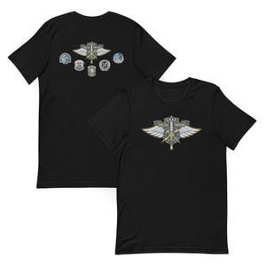 Può includere: T-shirt nere con un design della US Air Force Special Warfare. La parte anteriore della maglietta mostra un emblema dettagliato con ali, una spada e la scritta "USAF SPECIAL WARFARE". La parte posteriore della maglietta presenta ulteriori toppe militari.