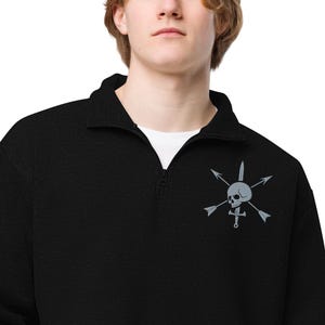 Op de afbeelding: Zwart sweatshirt met een kwartrits en een wit ondershirt. Het sweatshirt heeft een grijs ontwerp van een schedel en gekruiste botten met pijlen en een zwaard. De kraag is een opvouwbare stijl.