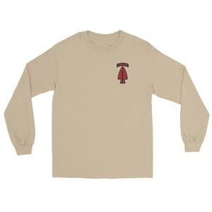 Pode incluir: Camiseta de manga comprida bege com um patch de ponta de flecha vermelha e a palavra "AIRBORNE" acima. A ponta da flecha é delineada em preto. A camisa é feita de um material macio e confortável.