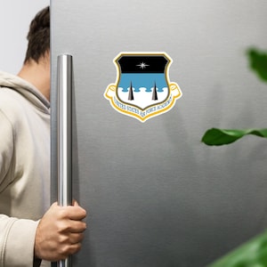 Puede incluir: Una pegatina con el emblema de la Academia de la Fuerza Aérea de los Estados Unidos. El emblema tiene forma de escudo con una parte superior negra, un centro azul claro y un borde amarillo. El texto "United States Air Force Academy" está escrito en círculo.
