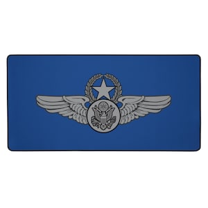 May include: A blue desk mat featuring a silver pilot's badge with a star, wings, and a circular emblem. The badge is centered on the mat, which has a black border. The design is a military aviation theme.