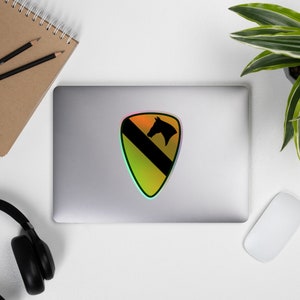 Könnte beinhalten: Ein holografischer Aufkleber mit dem Patch der 1. Infanterie-Division. Der Patch ist gelb und schwarz mit einem Pferdekopf in der Mitte.