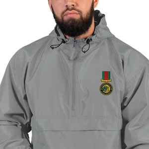 May include: A gray hooded anorak jacket with a half-zip closure and a drawstring hood. The jacket features a colorful embroidered patch on the chest. The patch has a green, yellow, and red design with text.