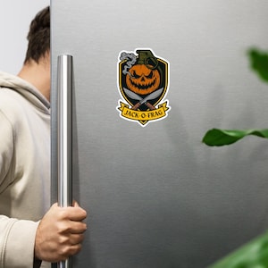 May include: A Halloween sticker design. It features a grinning jack-o'-lantern within a grenade shape, with crossed knives and smoke. The text "JACK-O-FRAG" is on a banner. The design is set against a black and yellow shield.