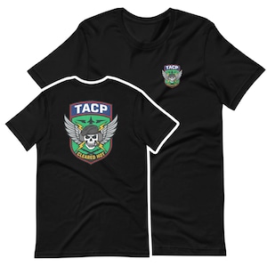 May include: Black T-shirts with a graphic design. One shirt displays a large emblem on the back with the text "TACP", a skull, wings, and the words "CLEARED HOT". The other shirt has a smaller emblem on the front.