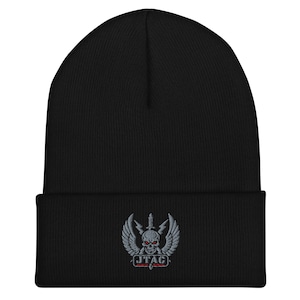 Op de afbeelding: Zwarte beanie muts met een geborduurd embleem. Het embleem toont een schedel met rode ogen, vleugels, een zwaard en de tekst "JTAC". De muts is gemaakt van zacht, gebreid materiaal, geschikt voor koud weer.