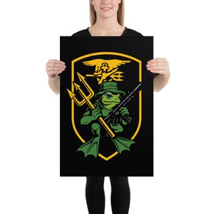 May include: Black poster featuring a cartoon frog in a green hat and flippers, holding a trident and a rifle. The frog is inside a yellow shield with a golden eagle and trident emblem. The background is black.