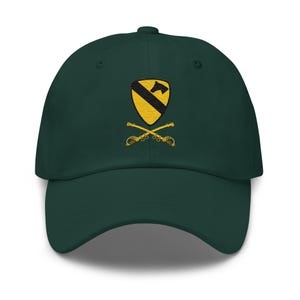 Peut inclure: Casquette de baseball vert foncé avec une visière incurvée. L'écusson brodé sur le devant présente un motif de bouclier jaune et noir avec des sabres jaunes croisés. La casquette est en tissu doux.