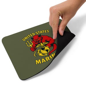 May include: Olive green mousepad featuring a red devil holding a trident, with the words "UNITED STATES MARINES" in yellow. The devil is positioned above a globe and eagle emblem. The mousepad has a black, textured underside.