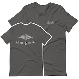 Peut inclure: T-shirt gris foncé avec un écusson détaillé sur le devant et une version plus petite sur la poitrine. L'écusson comprend des ailes, une épée et des motifs circulaires. Le t-shirt est en matière souple.