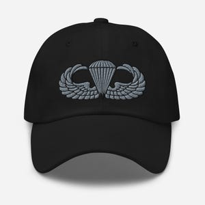 May include: Black baseball cap with a silver embroidered parachute and wing design. The cap has a curved brim and a structured fit. The embroidered emblem is centered on the front of the cap.