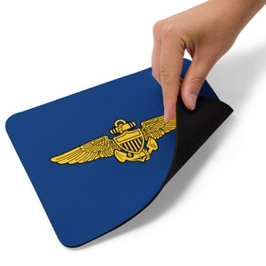 May include: A blue mouse pad with a gold naval aviator wings insignia. The mouse pad has a black rubber backing.