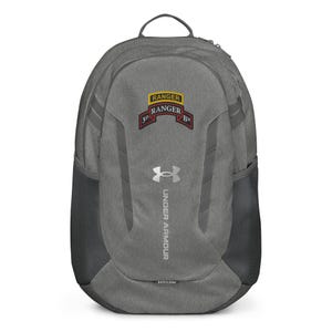 May include: A heather gray Under Armour backpack featuring a 3D Ranger Battalion patch on the upper front. The bag includes a silver logo, vertical dark gray accents, side mesh pockets, and a top handle. The text 3D RANGER BN is visible on the patch.