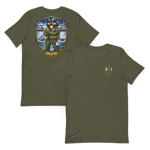 May include: Olive green t-shirts with a cartoon illustration of a pilot on the back and a smaller version on the front. The pilot illustration features a cartoon character in a flight suit with a military emblem.