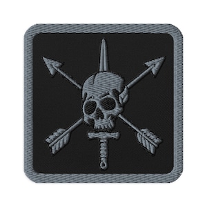 May include: Embroidered patch featuring a skull with a vertical spike, crossed arrows, and a dagger. The design is in shades of gray on a black square background with a gray border. Ideal for jackets, bags, or other apparel.