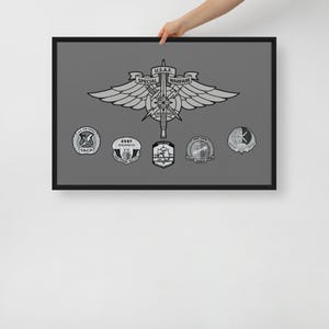 May include: Framed print featuring a gray background with a central emblem and several smaller badges. The main emblem reads "U.S.A.F. SPECIAL WARFARE" and includes wings, a sword, and a star. The smaller badges are circular and oval.