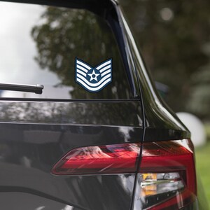 Peut inclure: Un autocollant d'insigne de grade de l'armée de l'air bleu et blanc avec cinq chevrons et une étoile, appliqué sur la lunette arrière d'une voiture noire.