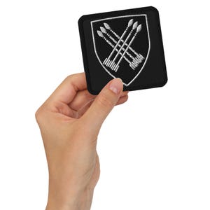 Peut inclure: Écusson brodé noir avec un bouclier blanc et des flèches croisées. L'écusson mesure environ 5 cm sur 5 cm.