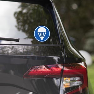May include: A blue and white parachute sticker on a black car. The sticker is a circle with a white parachute inside.