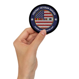 Könnte beinhalten: Ein runder, blau-schwarzer gestickter Aufnäher mit einem weißen Stern, einer amerikanischen Flagge und dem Text "Prevent Veteran Suicide, Choose Life, Never Quit".