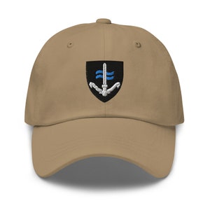 May include: A tan baseball cap with an embroidered patch featuring a black shield with a white anchor and blue waves, and a white sword.