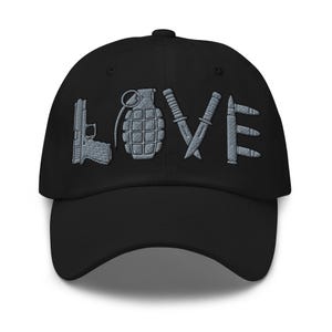 Puede incluir: Una gorra de béisbol negra con bordado gris en la parte frontal. El diseño forma la palabra LOVE, donde la letra L es una pistola, la O es una granada de mano, la V está formada por dos cuchillos cruzados y la E son tres balas apiladas.