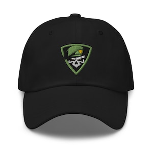 Peut inclure: Casquette de baseball noire avec un patch vert brodé représentant un crâne portant un béret vert. Le crâne a des yeux et des dents blancs.