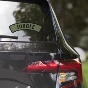 Peut inclure: Une voiture noire avec un autocollant vert et noir qui dit "JUNGLE" sur la vitre arrière.
