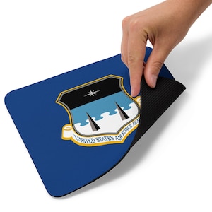 Può includere: Tappetino per mouse rettangolare blu con l'emblema dell'Accademia dell'Aeronautica Militare degli Stati Uniti. L'emblema ha la forma di uno scudo con una parte superiore nera, onde azzurre e due torri nere. Il testo "UNITED STATES AIR FORCE ACA" è in uno striscione giallo.