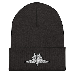 May include: A dark gray beanie with a white embroidered emblem of a winged dagger. The emblem is a stylized design with a dagger in the center and wings on either side.