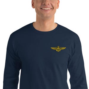 May include: A navy blue long-sleeved shirt with a gold emblem on the chest. The emblem depicts a shield, wings, and a crown. The shirt is made of a soft material and is suitable for casual wear.