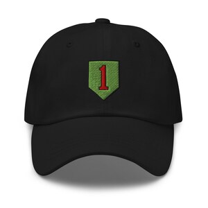 May include: A black baseball cap featuring an embroidered patch on the front. The patch is a light green shield shape with a dark red number one centered in the middle. The cap has a curved brim and a structured crown with a button on the top.