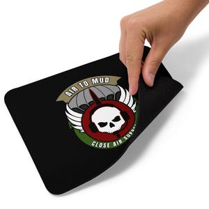 May include: Black rectangular mousepad with a circular emblem. The emblem features a skull wearing a headset, wings, and a parachute design. Text reads "AIR TO MUD" and "CLOSE AIR SUPPORT".