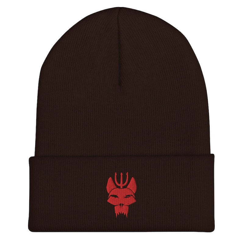 Puede incluir: Un gorro de punto marr&oacute;n con un logotipo bordado en rojo de una cabeza de animal estilizada con un tridente encima.