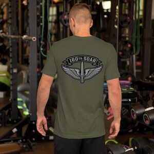 May include: Olive green t-shirt featuring a black and gray emblem on the back. The emblem includes the text "160th SOAR" above a design of wings and a sword.