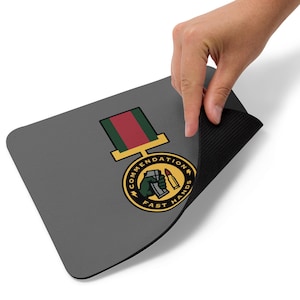 May include: Gray rectangular mousepad featuring a military-style medal design. The medal has a green and red ribbon and a gold border. The circular emblem reads "COMMENDATION FAST HANDS" with a hand holding a grenade and a bullet.