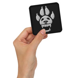 May include: Black embroidered patch with a white wolf paw print with a skull and fangs inside.