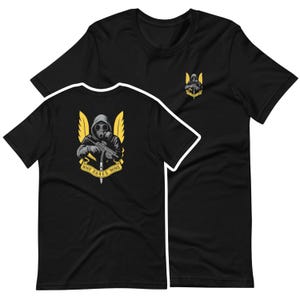 Op de afbeelding: Zwarte t-shirts met een afbeelding van een figuur met een gasmasker die een wapen vasthoudt, met gele vleugels en de tekst "WHO DARES WINS". Eén shirt heeft de afbeelding op de rug, de andere heeft een kleinere versie op de borst.