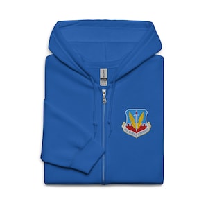 May include: A royal blue zip-up hoodie with a hood and an embroidered patch on the chest. The patch features a sword, wings, and the text "AIR COMBAT COMMAND". The hoodie has a full zip and a soft, comfortable appearance.